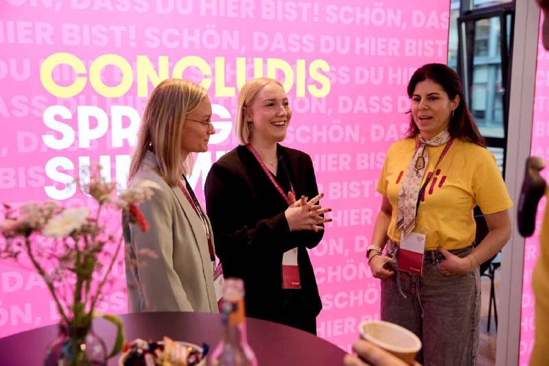 Drei Teilnehmerinnen im Gespräch vor dem concludis Spring Summit Backdrop